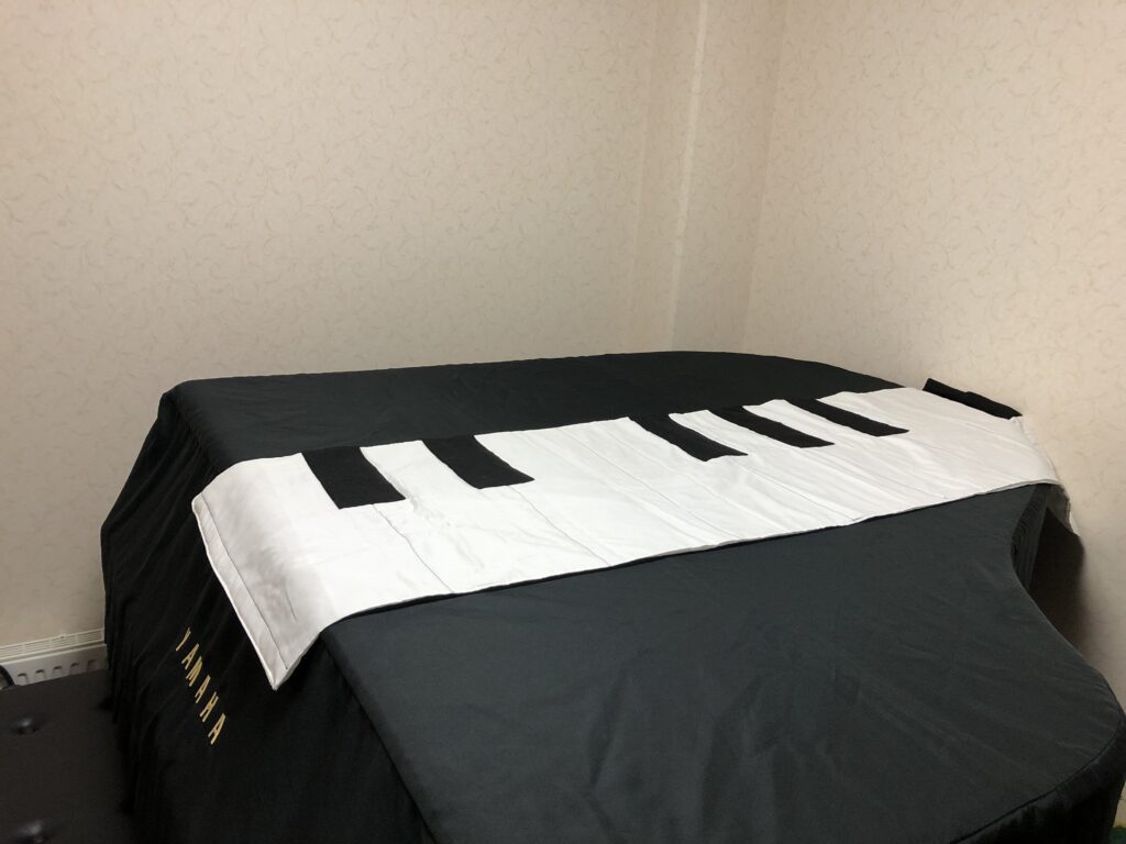 レッスン室のグランドピアノと手作りの大きな布鍵盤｜体を使って音程やリズムを楽しく学べる工夫いっぱいの環境